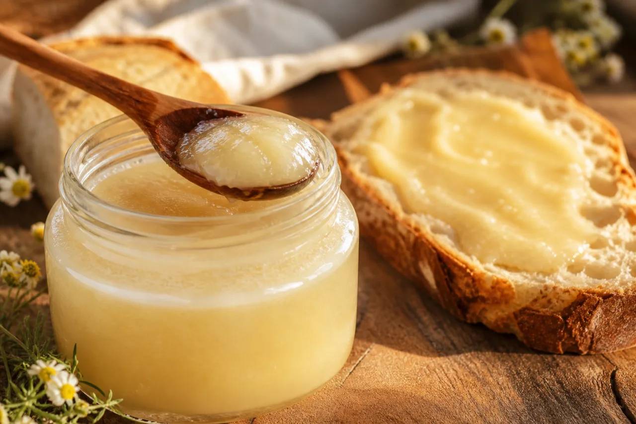 Geöffnetes Glas mit cremig gerührtem Honig und Holzlöffel